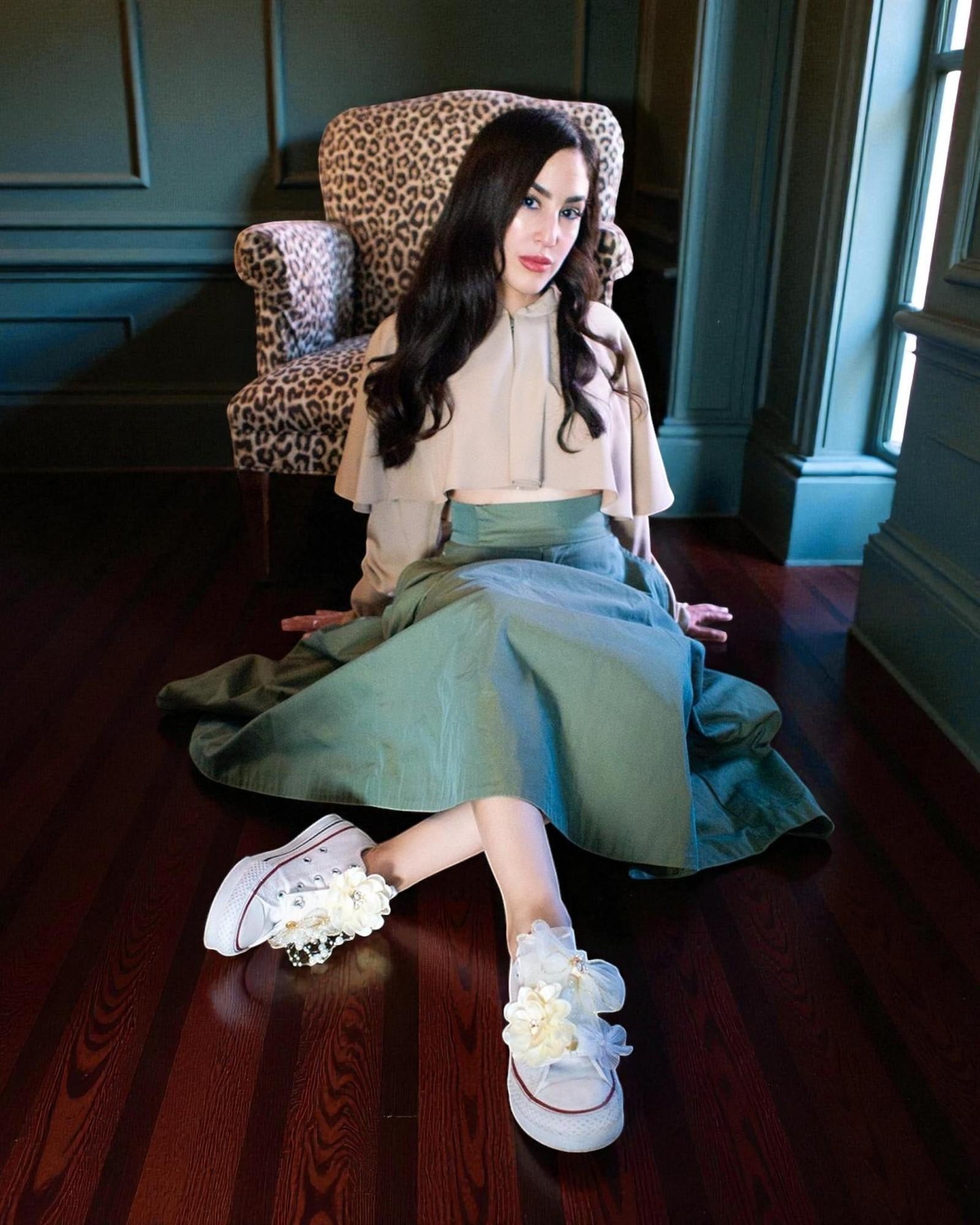 LŪPZ Champaign shoe accessories styled on white converse shoes, shown on a model seated on a hardwood floor in front of an upholstered chair